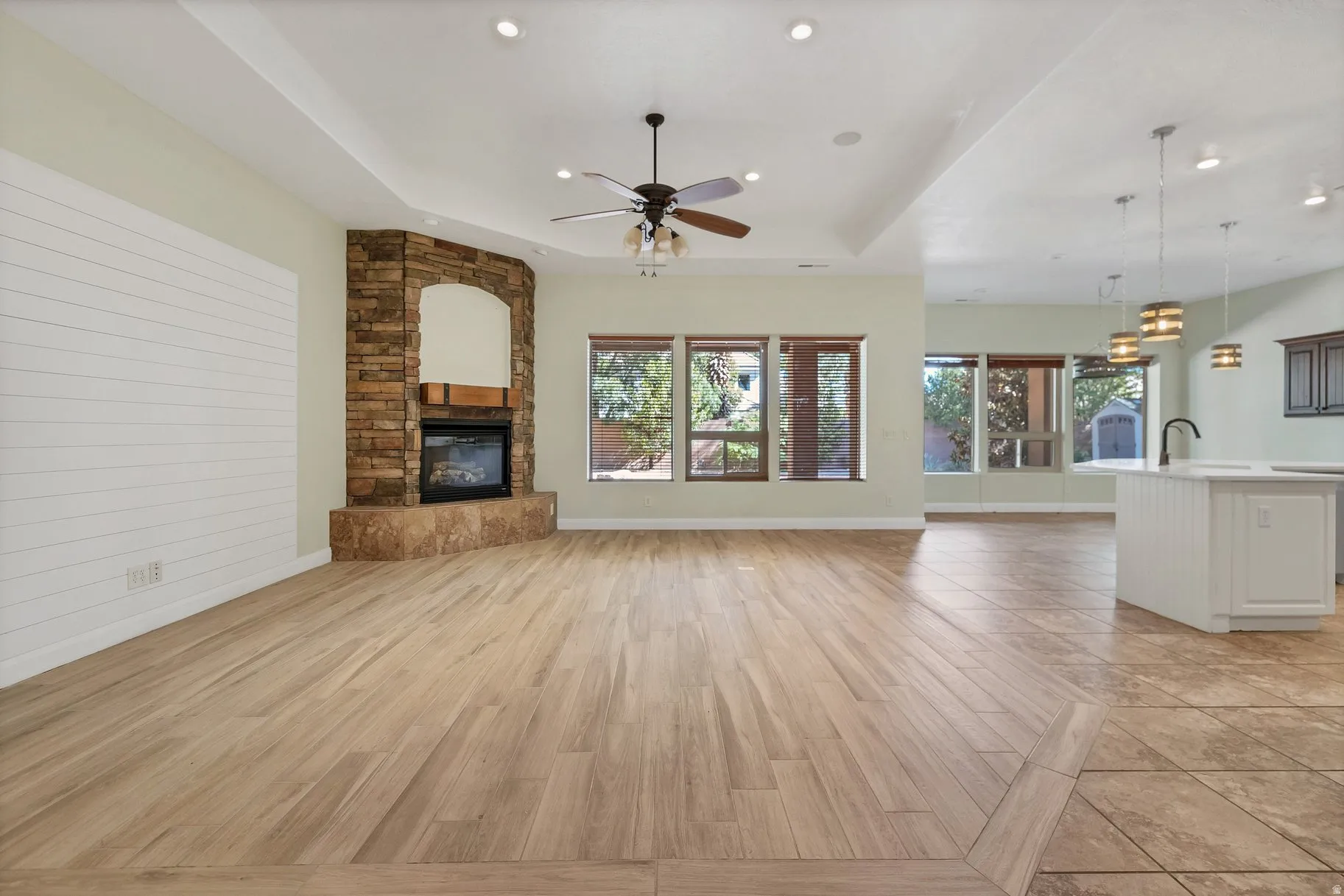 Unfurnished living room featuring a fireplace, a raised ceiling, light wood finished floors, ceiling fan, and recessed lighting