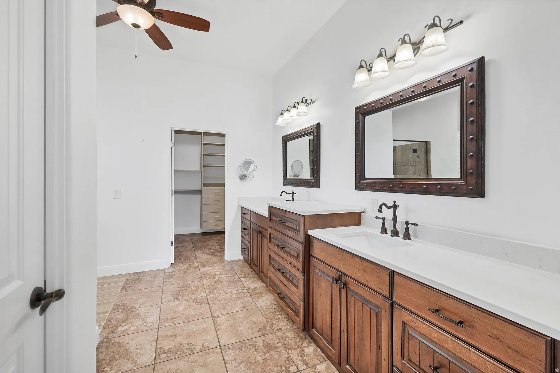 Bathroom with two vanities, a walk in closet, and a ceiling fan