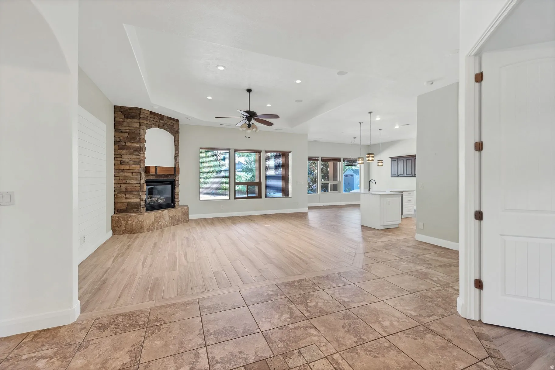 Unfurnished living room with a fireplace, a tray ceiling, a ceiling fan, light wood finished floors, and hanging lights