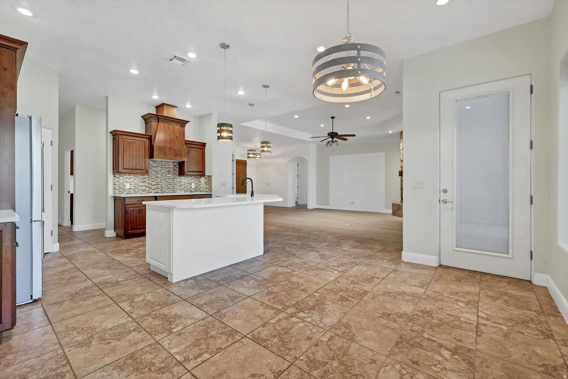 Kitchen with wood finish cabinets, arched walkways, an island with sink, open floor plan, and a chandelier