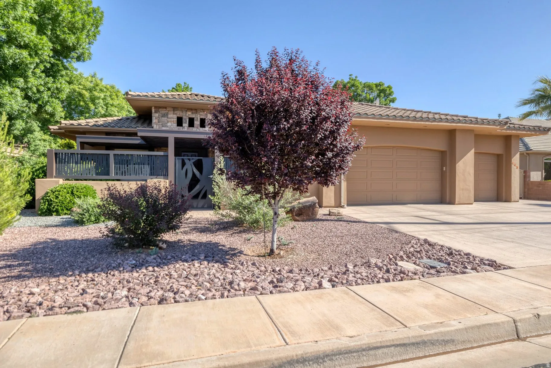View of front of property featuring a garage, concrete driveway, a tile roof, stone siding, and stucco siding