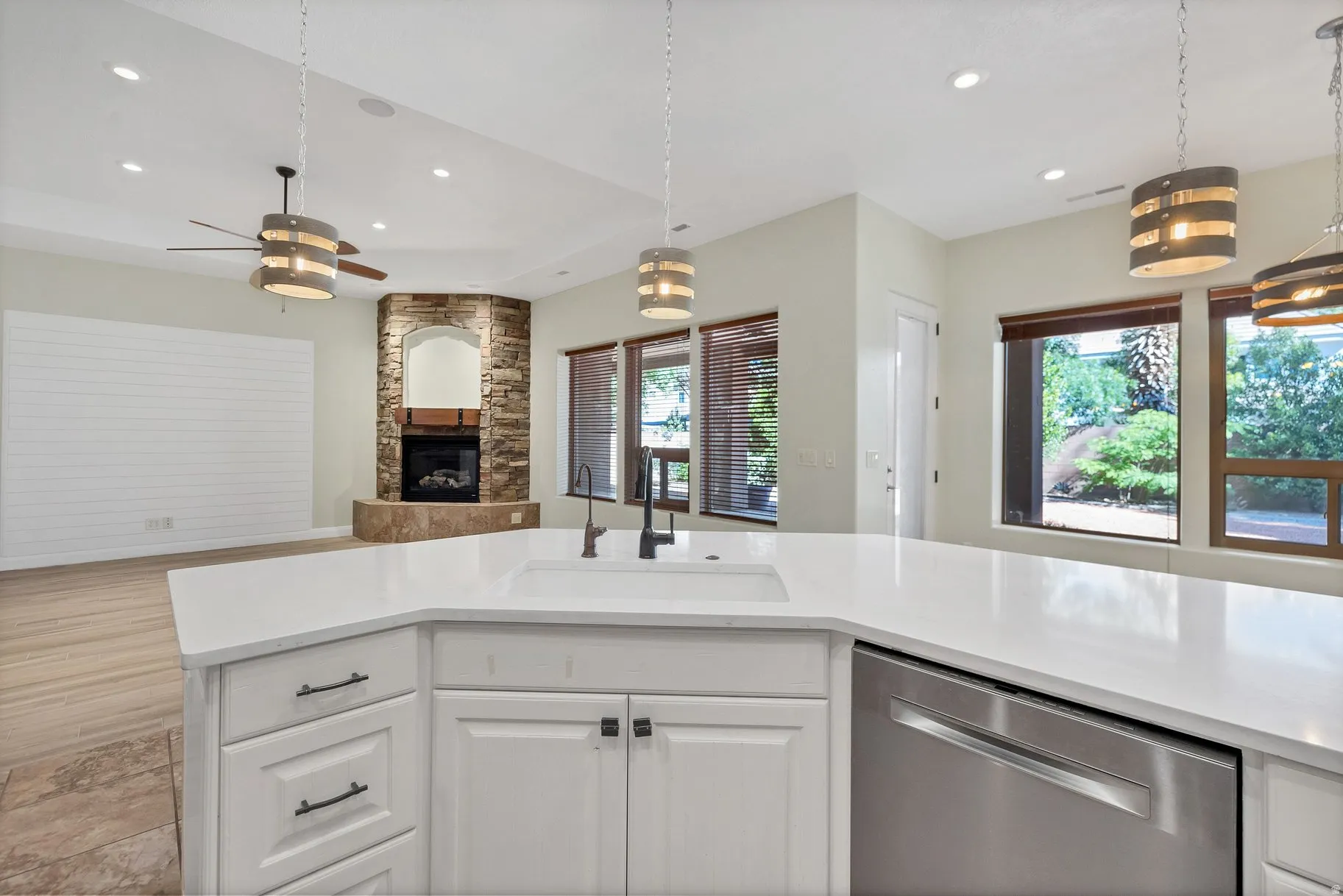 Kitchen featuring dishwasher, open floor plan, a stone fireplace, white cabinetry, and light stone countertops