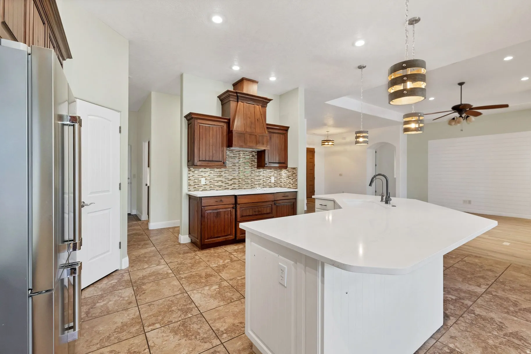 Two tone kitchen featuring freestanding refrigerator, a ceiling fan, a large island with sink, arched walkways, and light stone counters