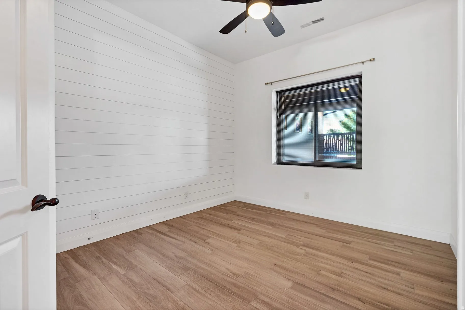 Empty room with light wood finished floors, a ceiling fan, and wood walls