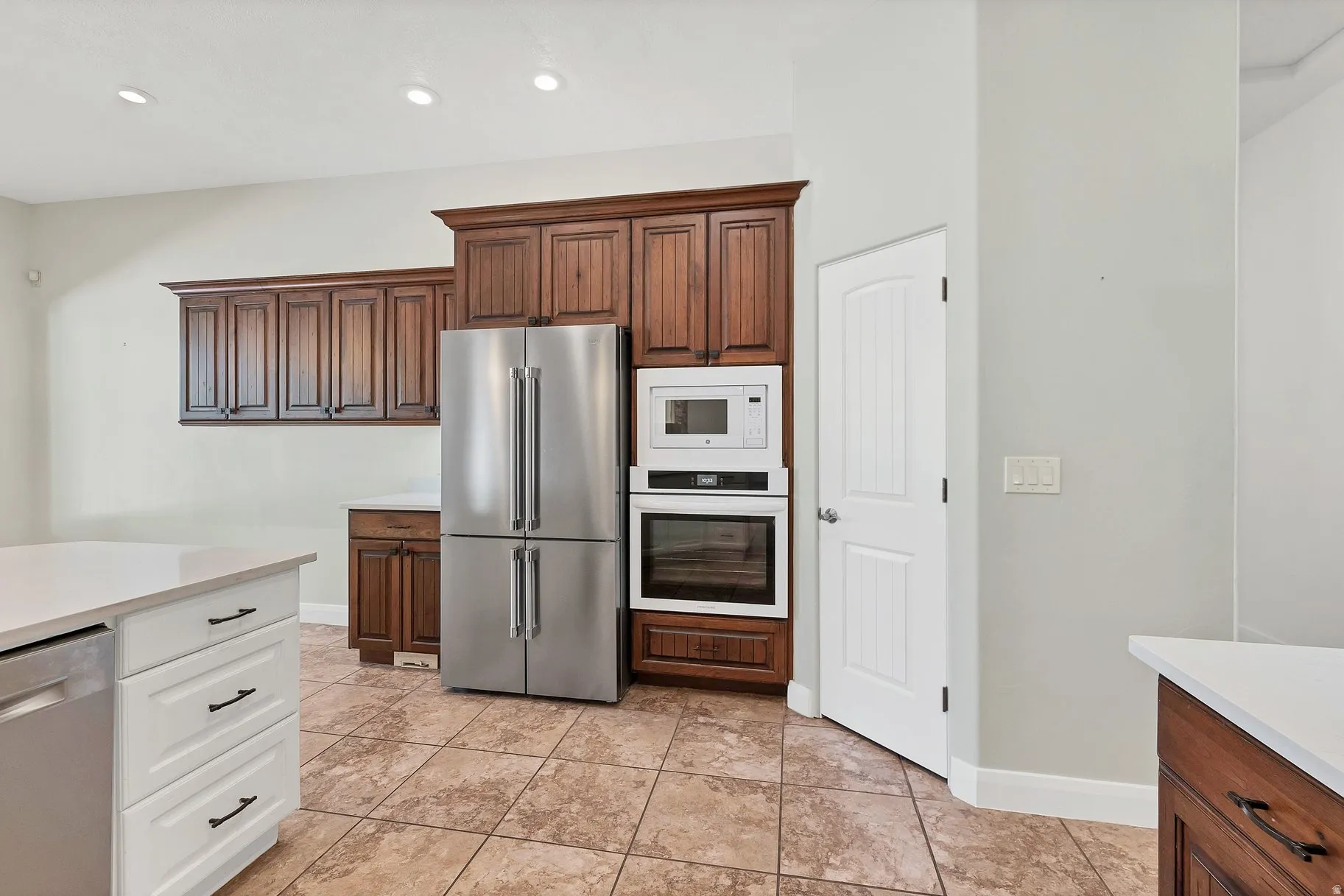 Two tone kitchen featuring stainless steel appliances, recessed lighting, two tone cabinetry, light tile patterned flooring, and light stone counters