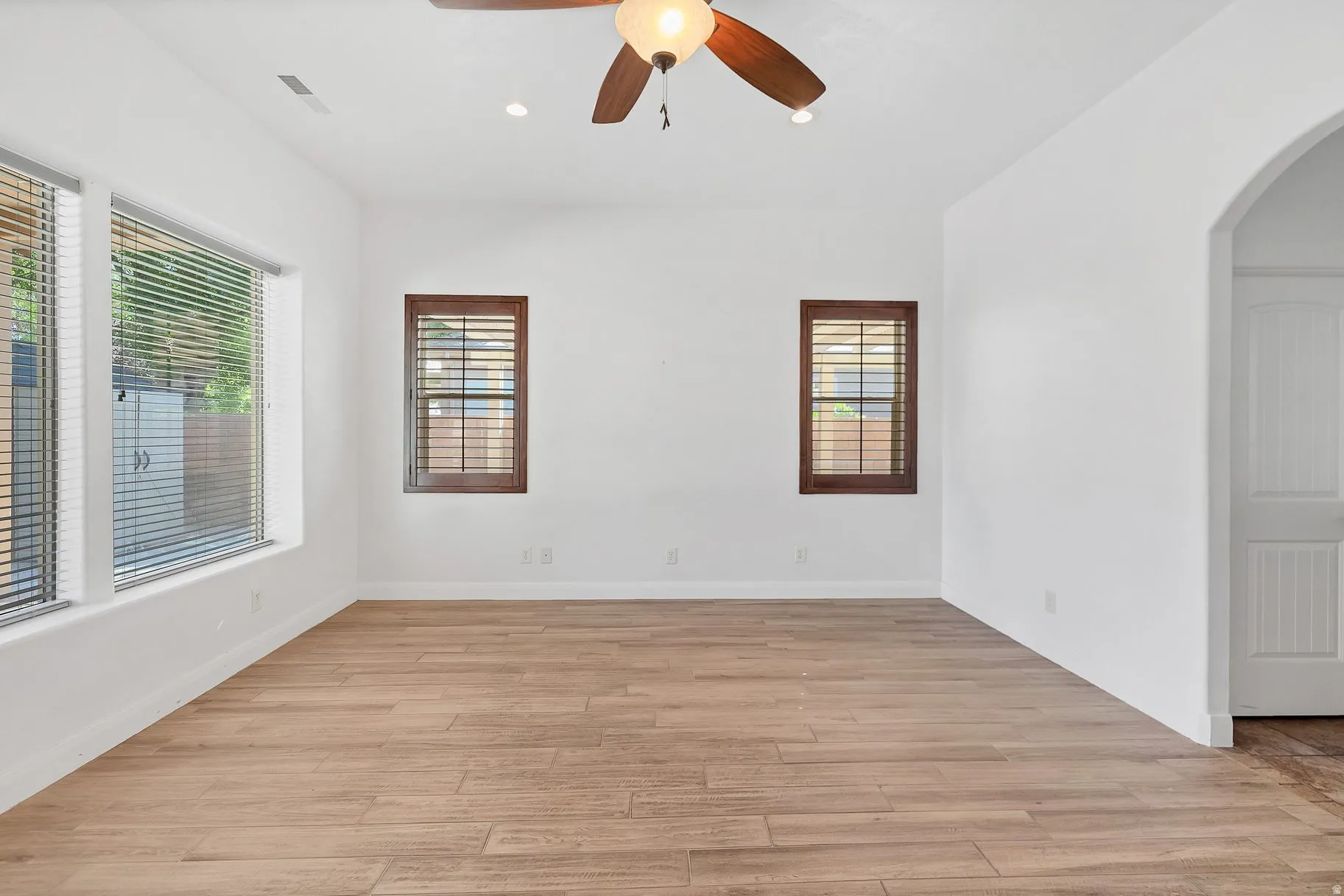 Spare room featuring ceiling fan, arched walkways, light wood-type flooring, and recessed lighting