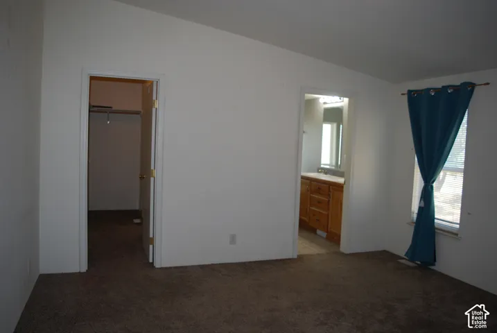 Carpeted room featuring a window with blinds, a doorway to a closet with shelving, and a doorway revealing a bathroom vanity with a mirror