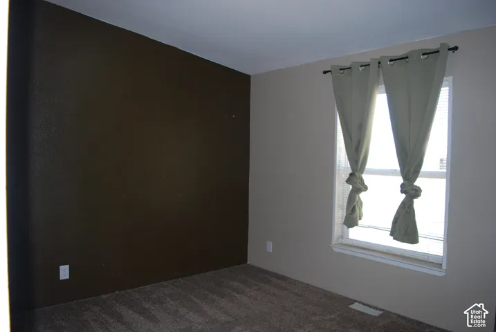 Room featuring a single window, a textured accent wall, and neutral-toned carpet flooring