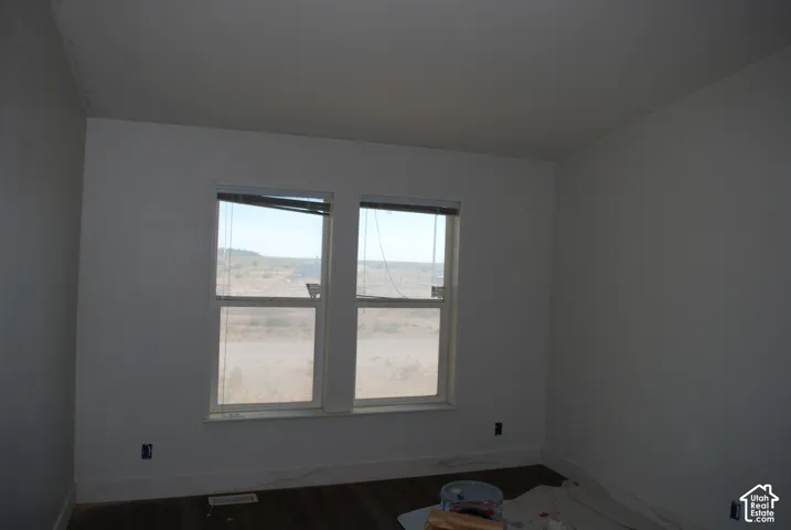 Room with two windows, white walls, dark wood-finish flooring, and white baseboards