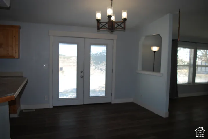 French doors with integrated blinds opening to an exterior, dark wood-finish flooring, a contemporary chandelier, a kitchen counter with wood cabinetry, and a wall partition with an arched pass-through window