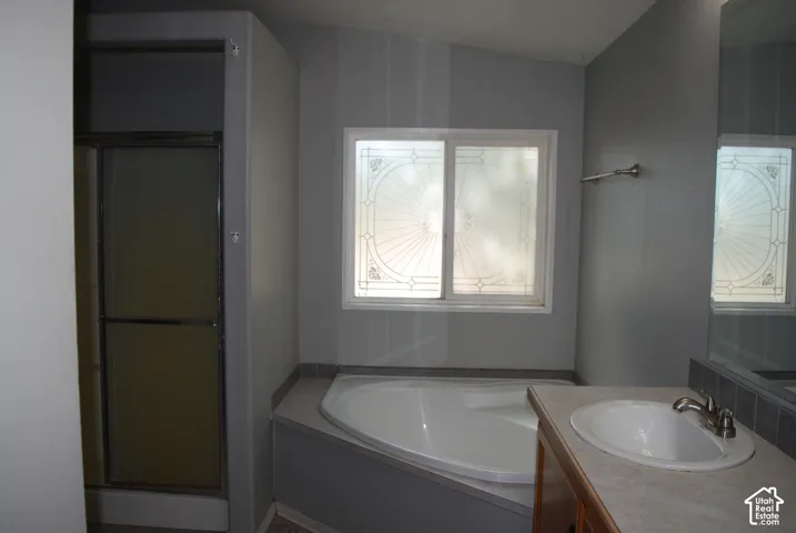 Bathroom featuring a built-in corner tub, a single vanity with an oval sink, an integrated countertop, and a sliding glass shower enclosure
