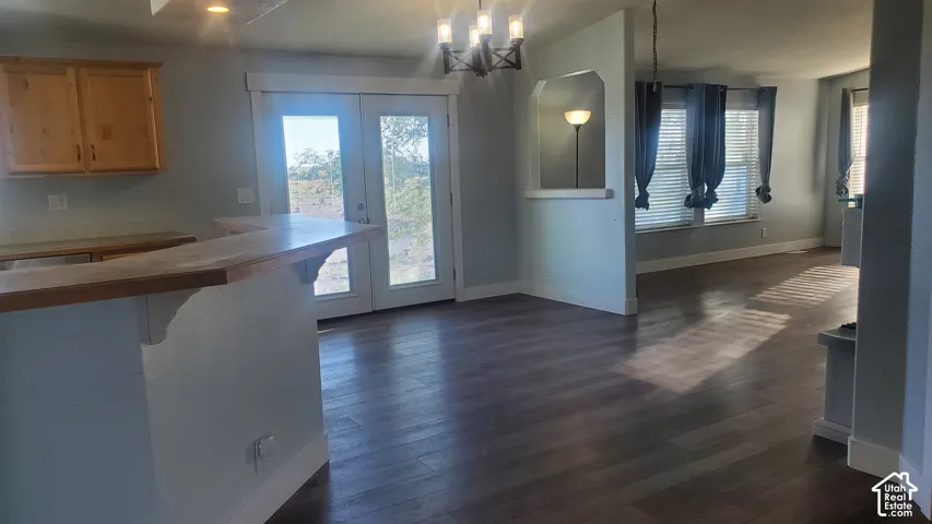 Wood-finish flooring, light wood cabinetry, double glass doors, a decorative chandelier, and an arched wall feature