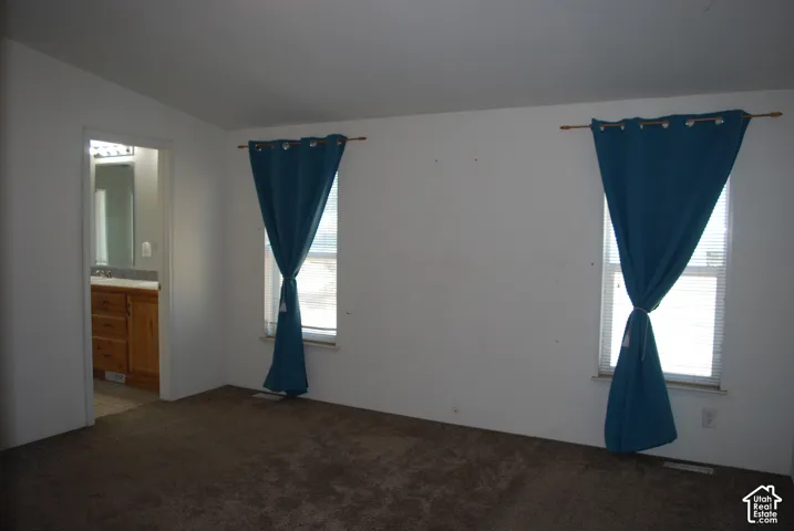 Carpeted room with two windows featuring blinds and an entryway to an attached bathroom