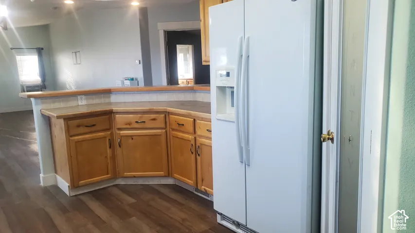 Kitchen featuring wood-finish flooring, wood cabinetry with dark hardware, a white side-by-side refrigerator, and a pantry with a brass doorknob