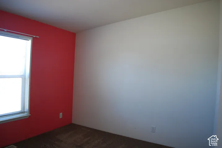 Room with a window featuring horizontal blinds, a red accent wall, and light-colored carpet flooring