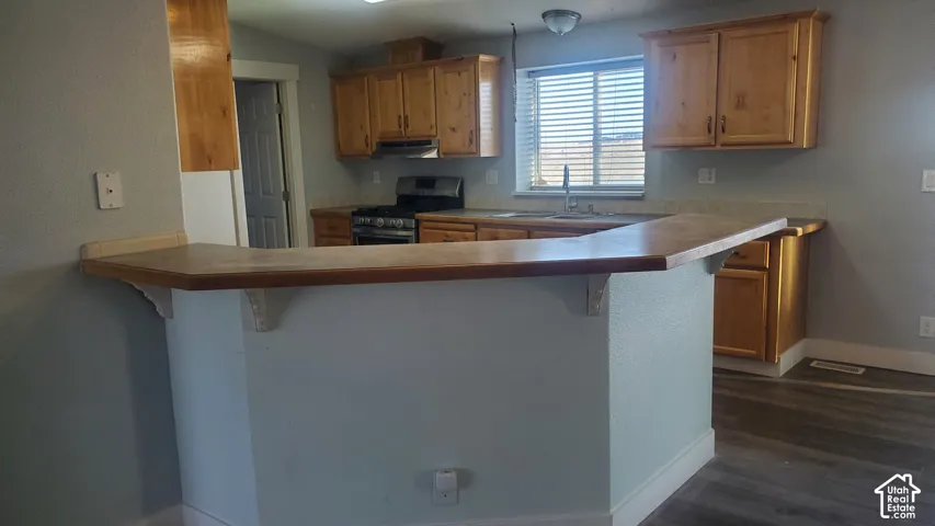 Kitchen featuring wood-finish cabinetry, stainless steel range with overhead microwave, a breakfast bar, and wood-finish flooring