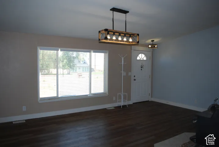 Open-concept room featuring wood-finish flooring, a white front door with an arched window, and a modern rectangular chandelier