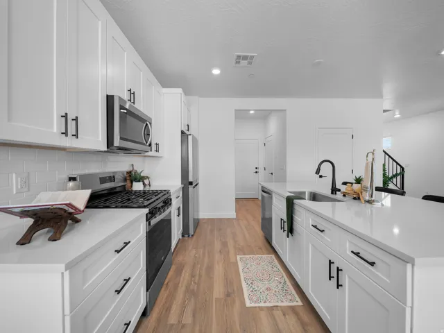 Modern kitchen featuring white shaker cabinetry, stainless steel appliances, light-toned countertops, a subway tile backsplash, and wood-finish flooring