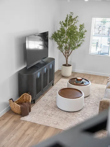 Wood-finish flooring with a neutral area rug, bright white walls, and a window with horizontal blinds