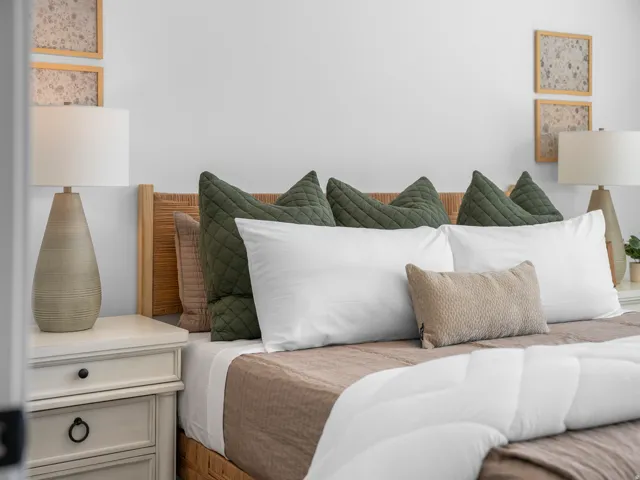 White painted walls, light wood headboard, and a three-drawer nightstand with dark hardware
