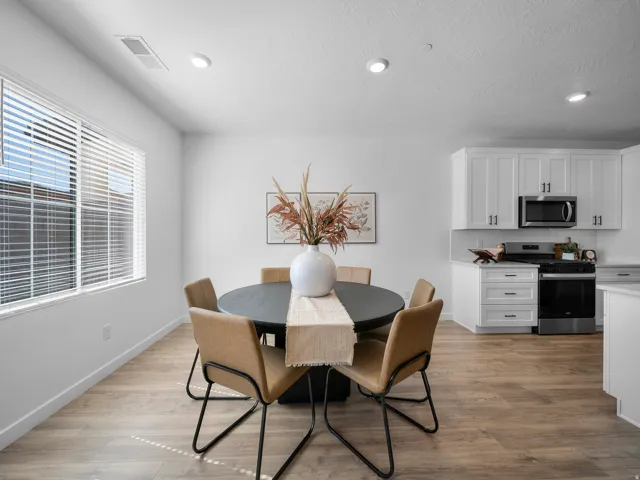 Wood-finish flooring, recessed lighting, white window blinds, white kitchen cabinetry with black hardware, and stainless steel appliances