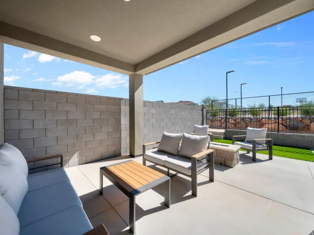 Covered concrete patio with recessed lighting, bordered by a block wall and artificial turf, featuring a built-in fire pit