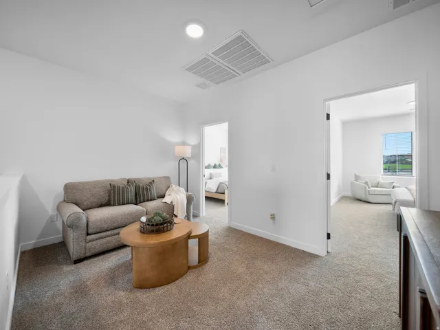 Carpeted area with recessed lighting, white walls, and a door opening into an additional room