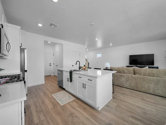 Open-concept living space featuring wood-finish flooring, recessed lighting, white cabinetry with black hardware, and a center island with an integrated sink