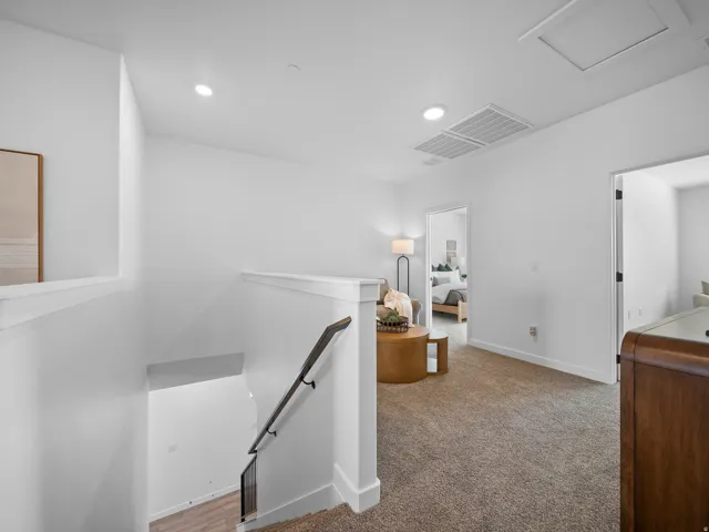 Carpeted hallway with recessed lighting and a white handrail leading to a lower level