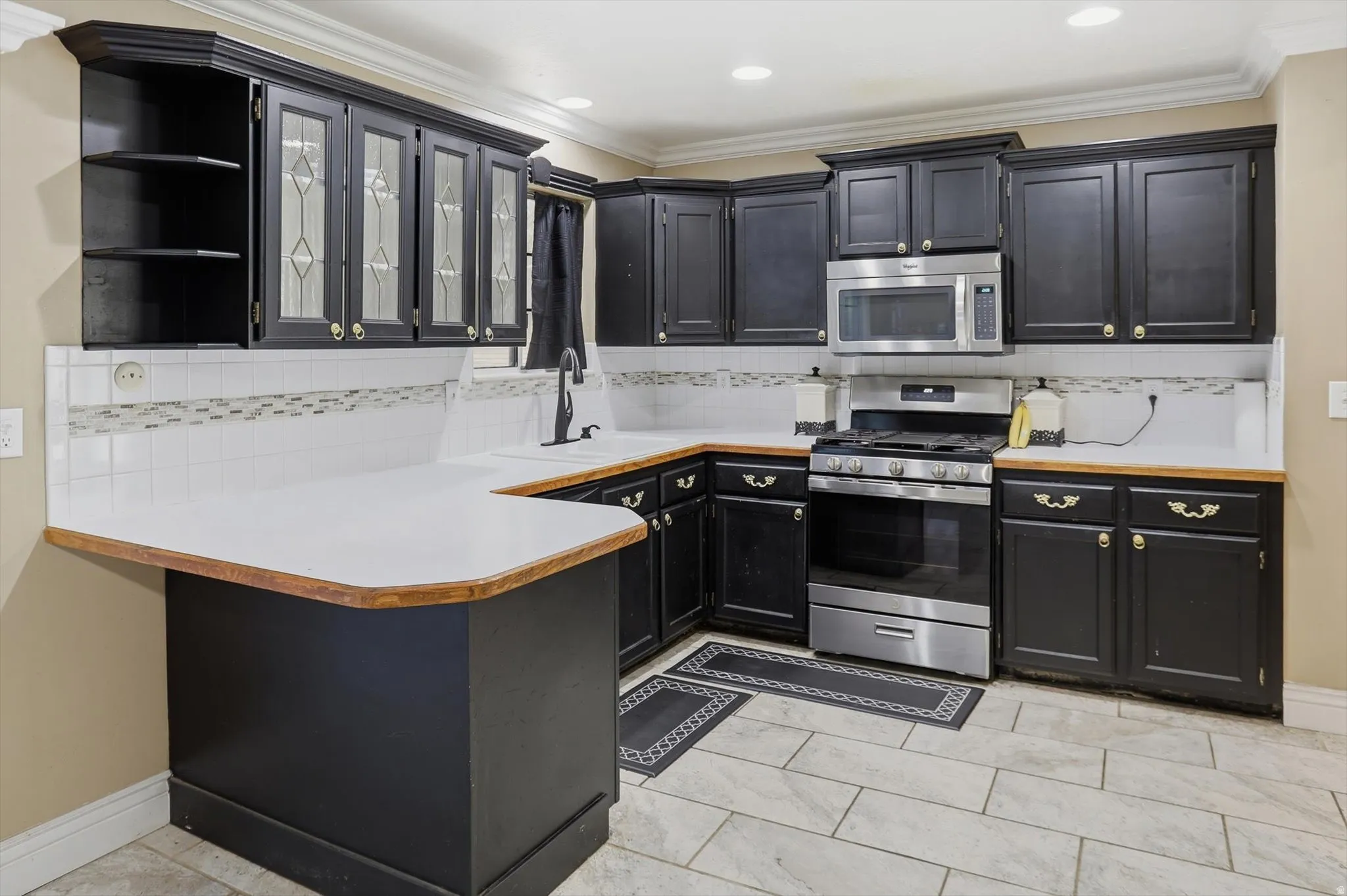 Kitchen featuring light countertops, stainless steel appliances, glass insert cabinets, dark cabinets, and tasteful backsplash