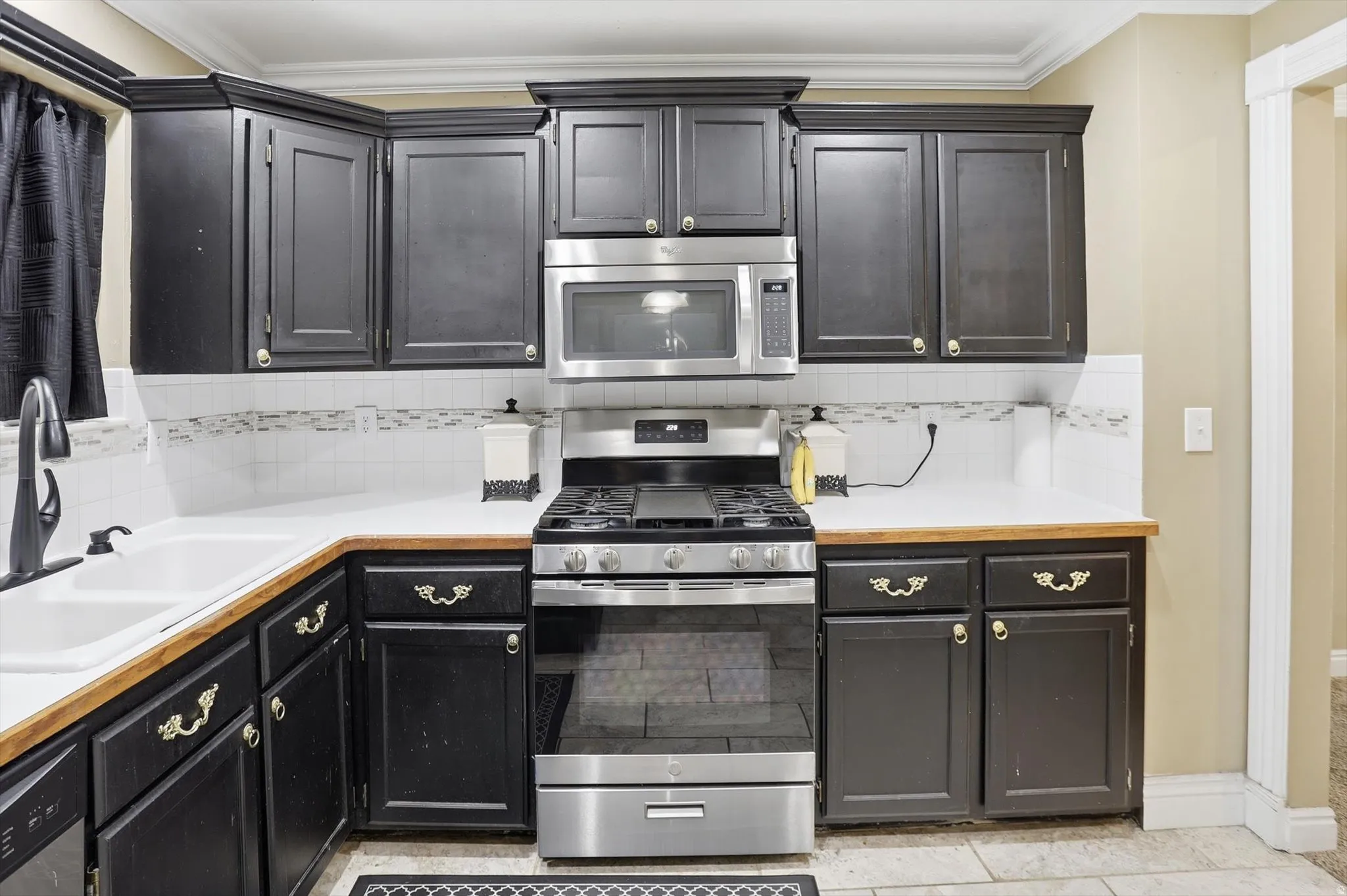 Kitchen featuring stainless steel appliances, light countertops, tasteful backsplash, dark cabinets, and light tile patterned flooring