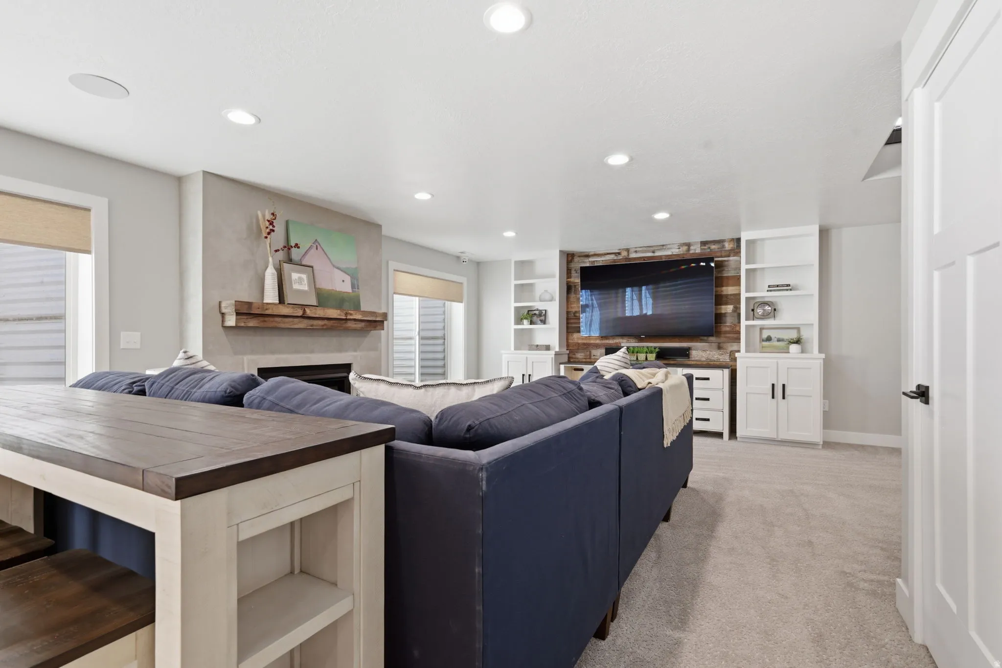 Living room with a fireplace, light colored carpet, built in shelves, and recessed lighting