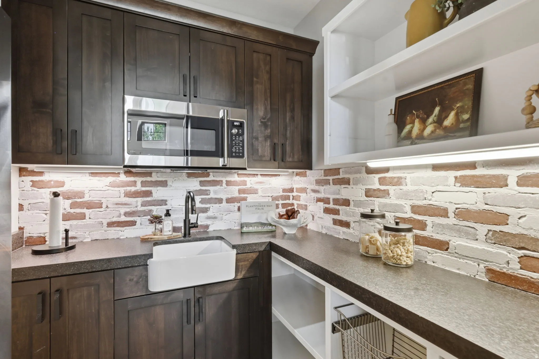 Kitchen with dark wood finish cabinetry, stainless steel microwave, tasteful backsplash, open shelves, and dark stone counters