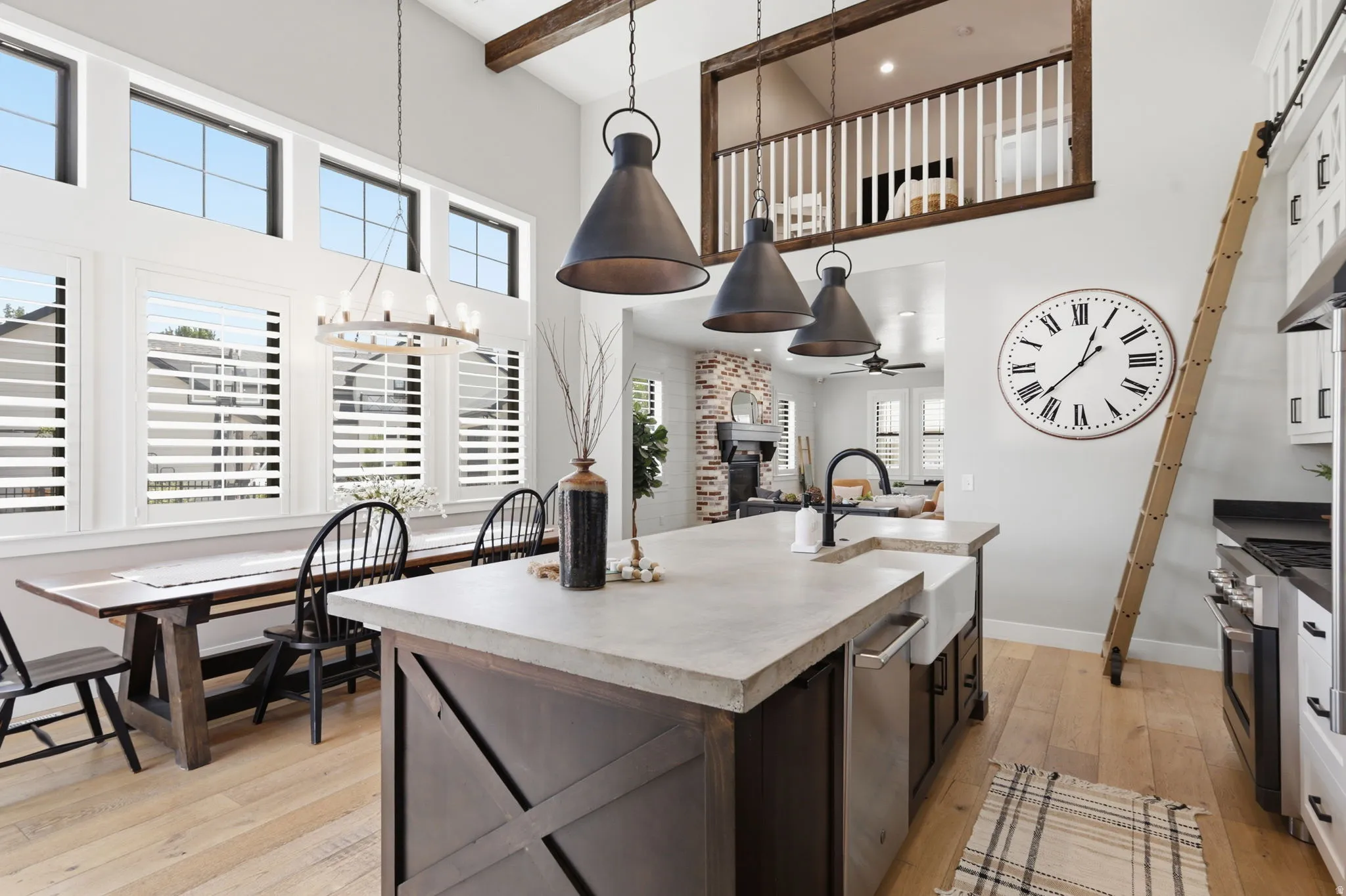 Dual tone kitchen with light wood-style floors, a center island with sink, stainless steel appliances, a high ceiling, and suspended lighting