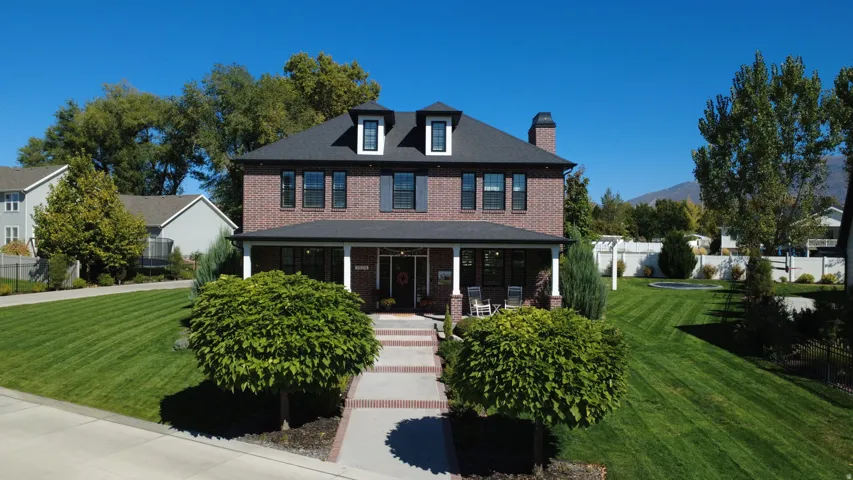 View of front of home with a front yard, a porch, brick siding, and a chimney