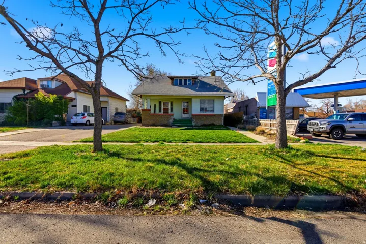 View of front of property featuring covered porch, brick siding, a chimney, and a front yard