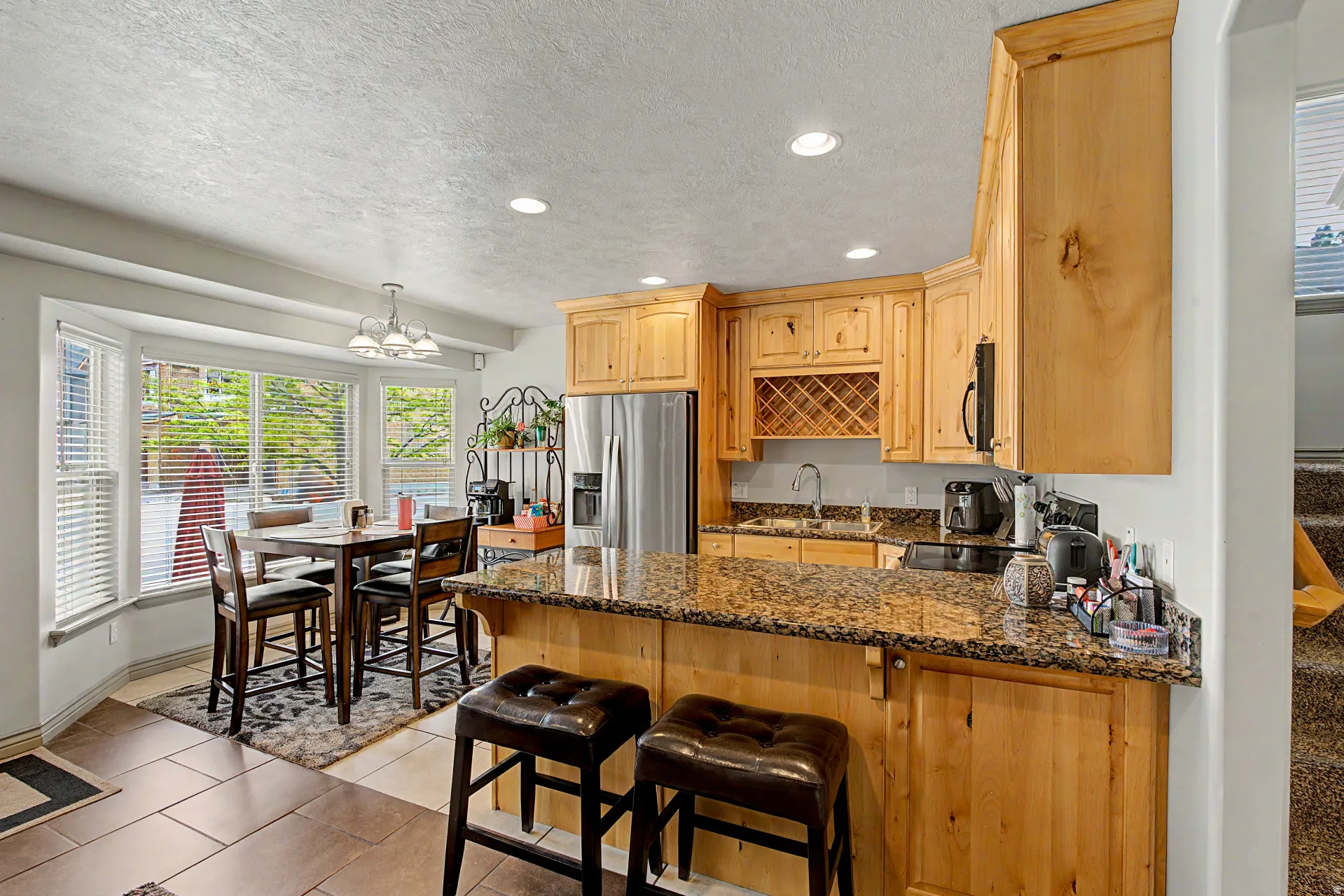 Kitchen with light wood finish cabinets, a peninsula, stainless steel appliances, a breakfast bar area, and dark granite countertops
