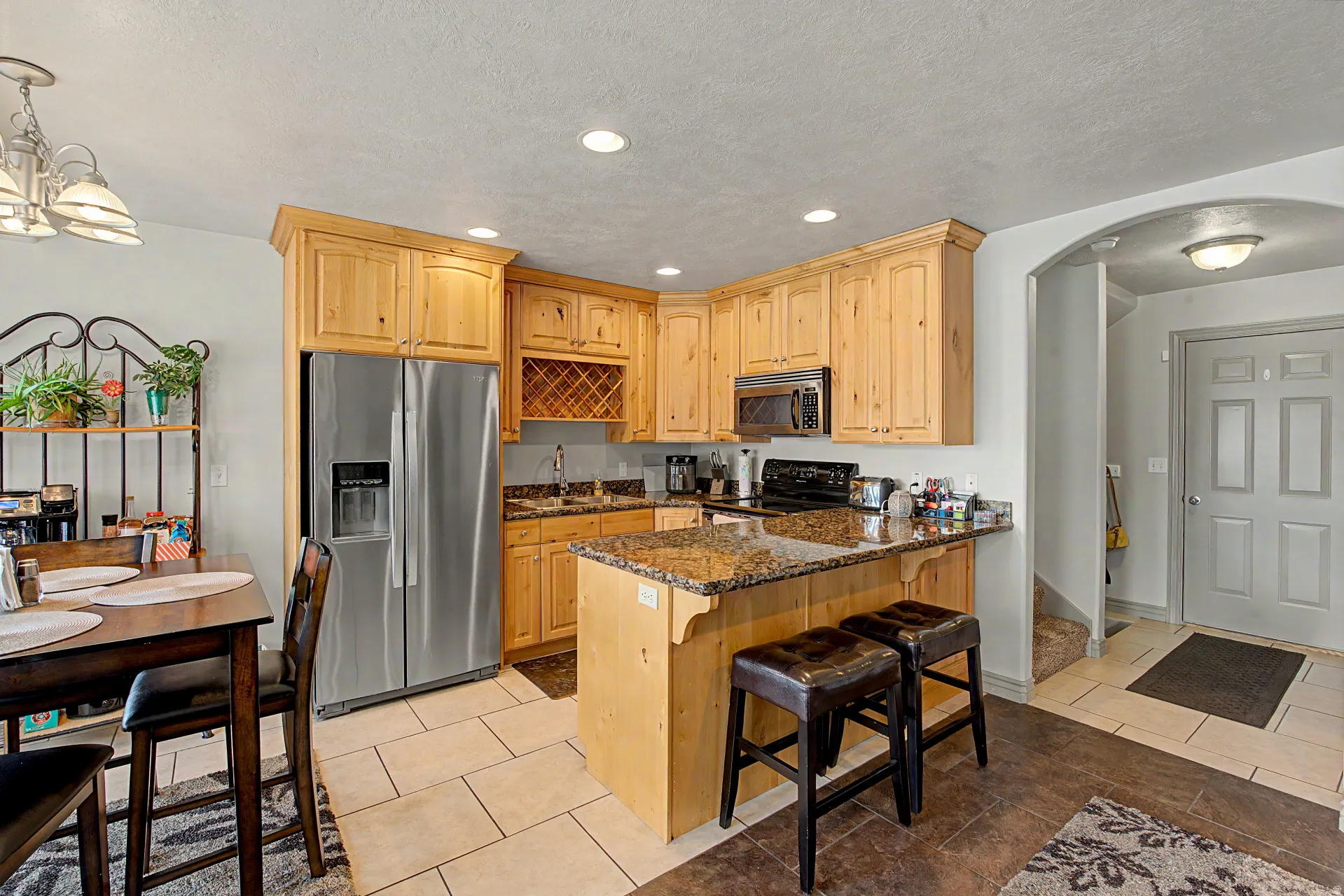Kitchen with arched walkways, stainless steel appliances, dark stone countertops, a breakfast bar, and light wood finish cabinets