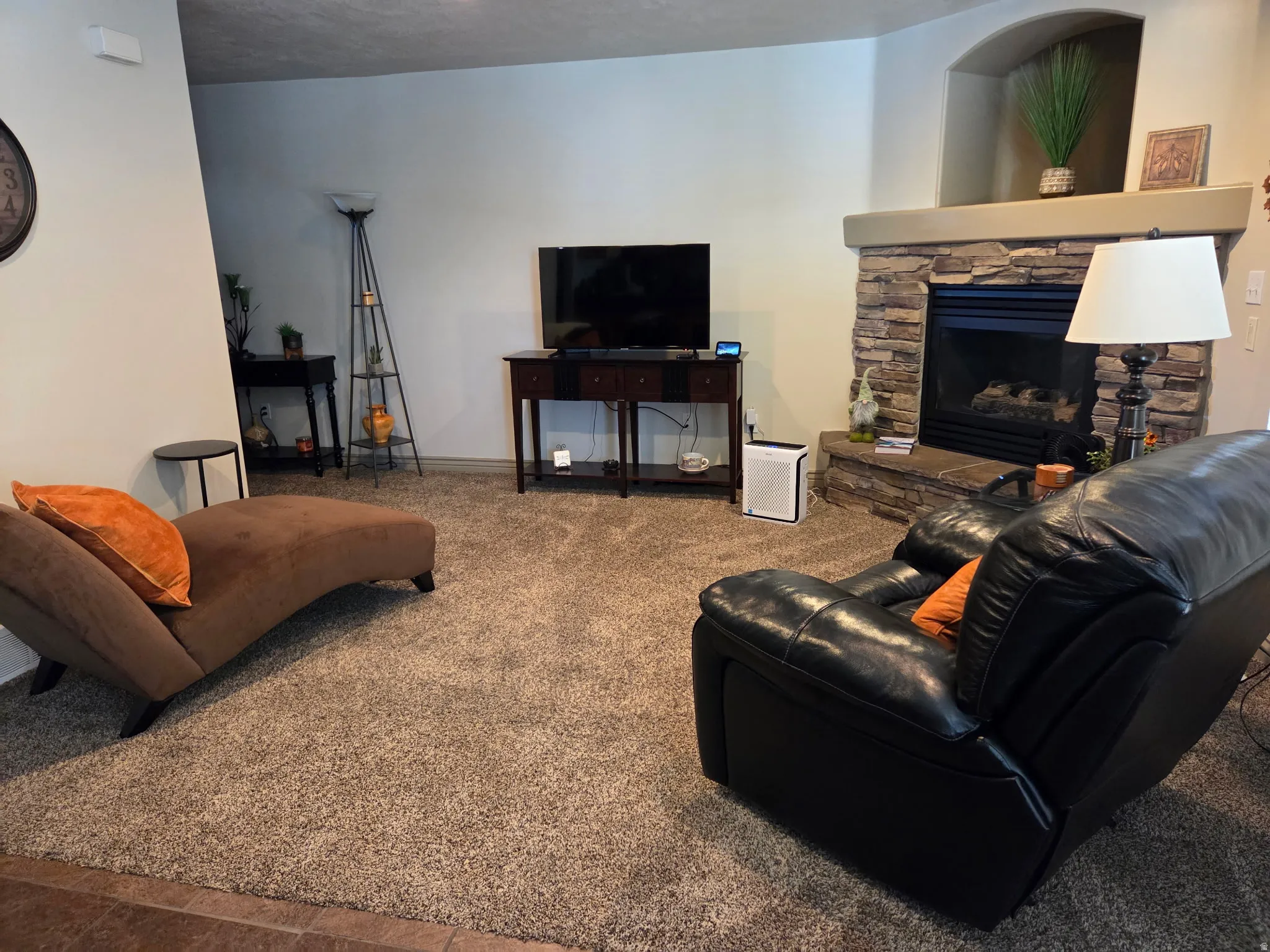 Living area featuring a stone fireplace with a raised hearth, a mantle with an arched niche, light-colored walls, and textured carpeting