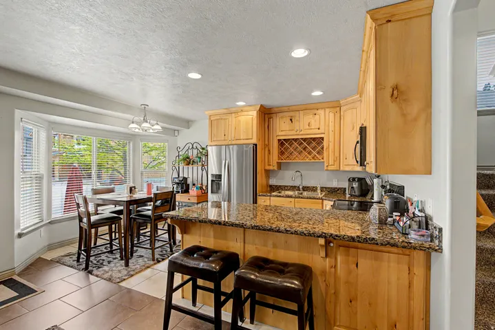 Kitchen with light wood finish cabinets, a peninsula, stainless steel appliances, a breakfast bar area, and dark granite countertops