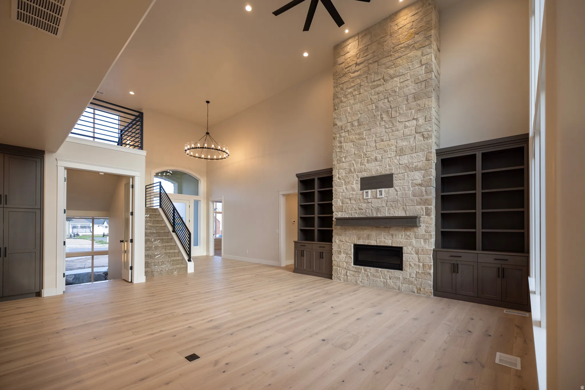 Unfurnished living room featuring a high ceiling, a stone fireplace, light wood-style tile floors, a ceiling fan, and suspended lighting