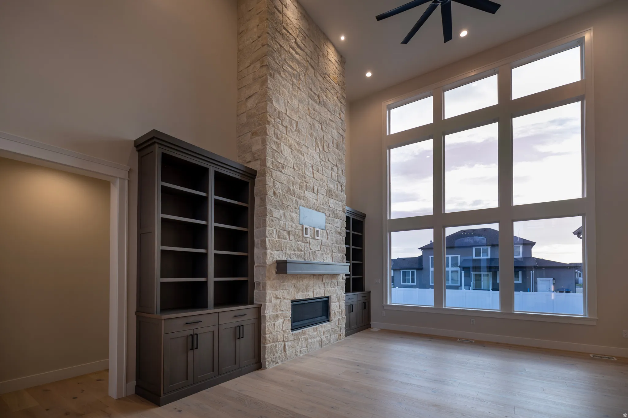 Unfurnished living room with a high ceiling, a stone fireplace, a ceiling fan, light wood-style tile floors, and recessed lighting