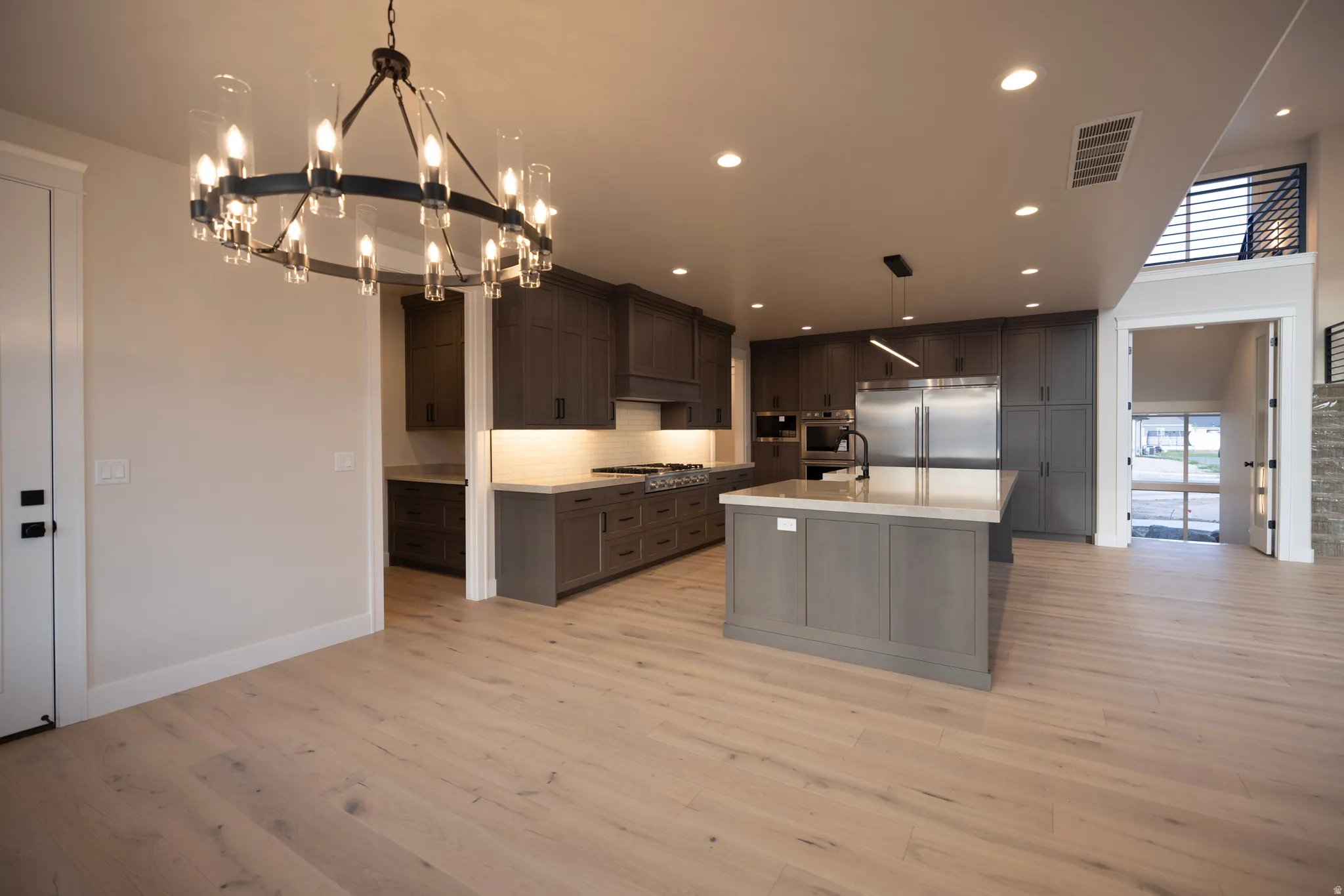 Kitchen featuring stainless steel appliances, an island with sink, light wood finished floors, suspended lighting, and decorative backsplash