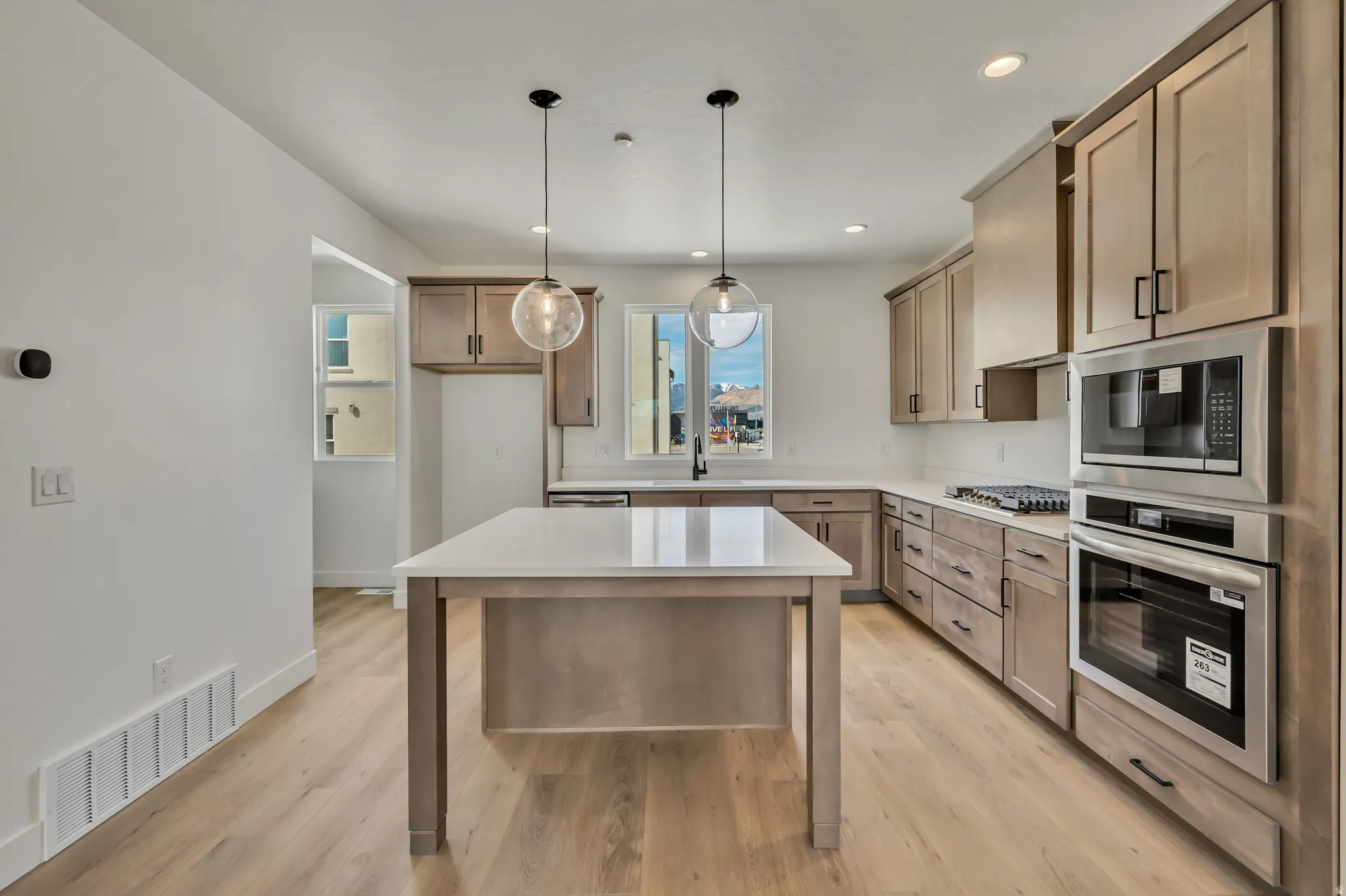 Kitchen with stainless steel appliances, light wood-type flooring, pendant lighting, wood finish cabinets, and light stone counters