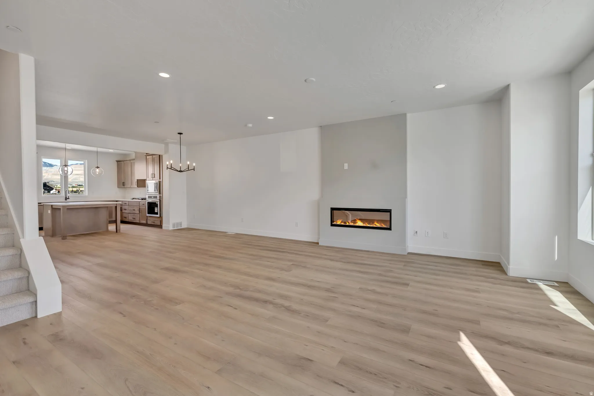 Unfurnished living room featuring a glass covered fireplace, suspended lighting, and light wood-type flooring