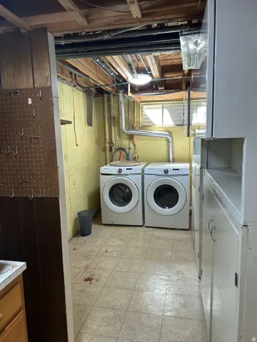 Laundry area featuring two front-loading machines, tiled flooring, built-in cabinetry, and exposed ceiling joists