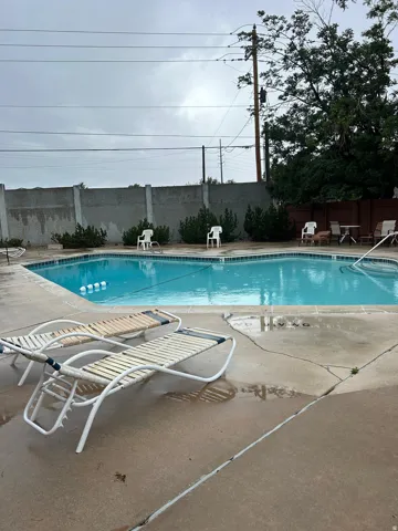 HOA Outdoor swimming pool with concrete surround, featuring a solid perimeter fence and mature landscaping