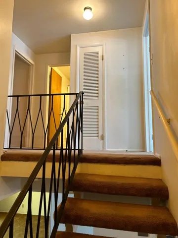 Staircase with brown carpeted treads and risers, featuring a black wrought iron railing and a painted wood handrail