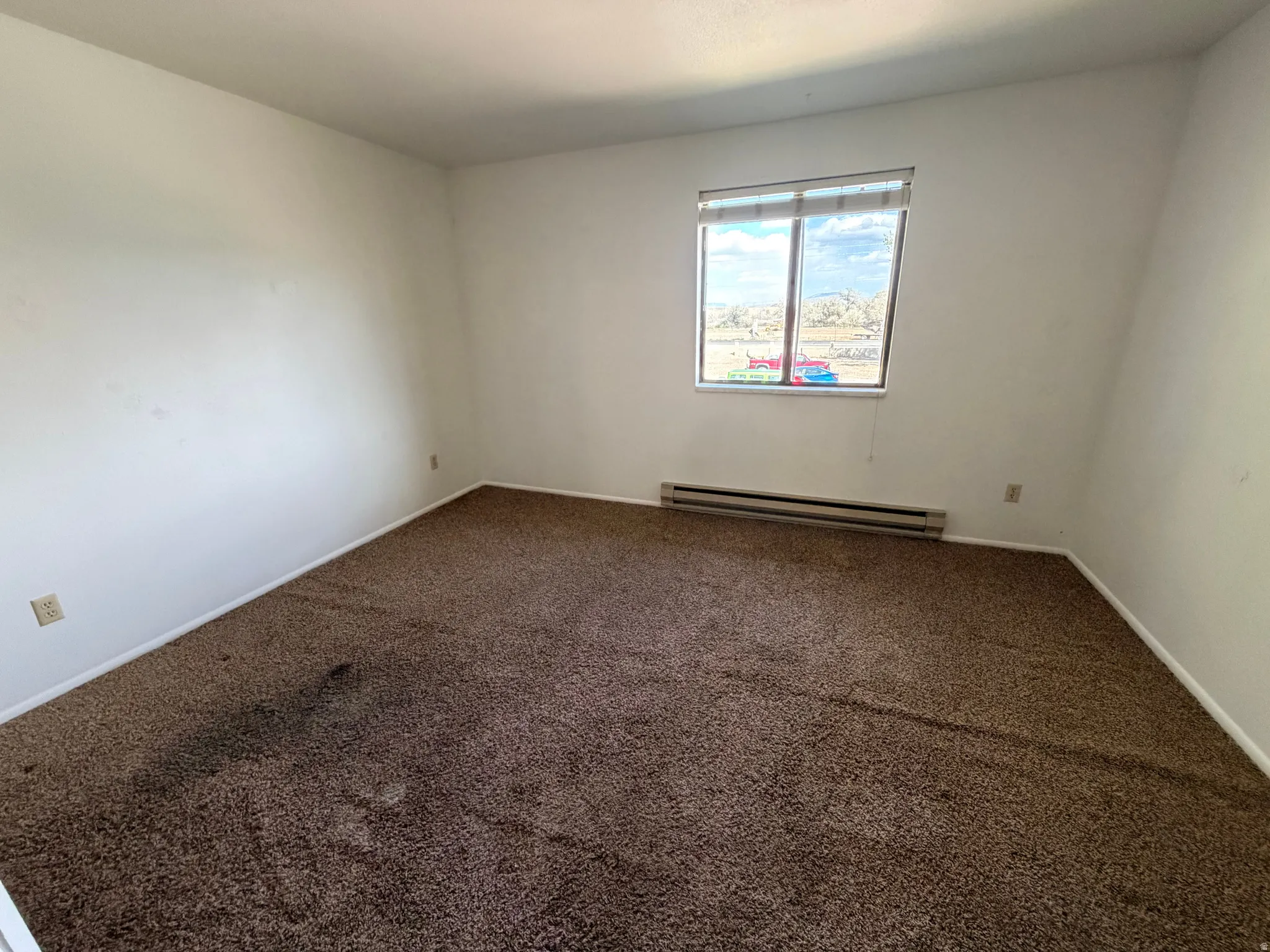 Unfurnished room featuring dark colored carpet and a baseboard radiator
