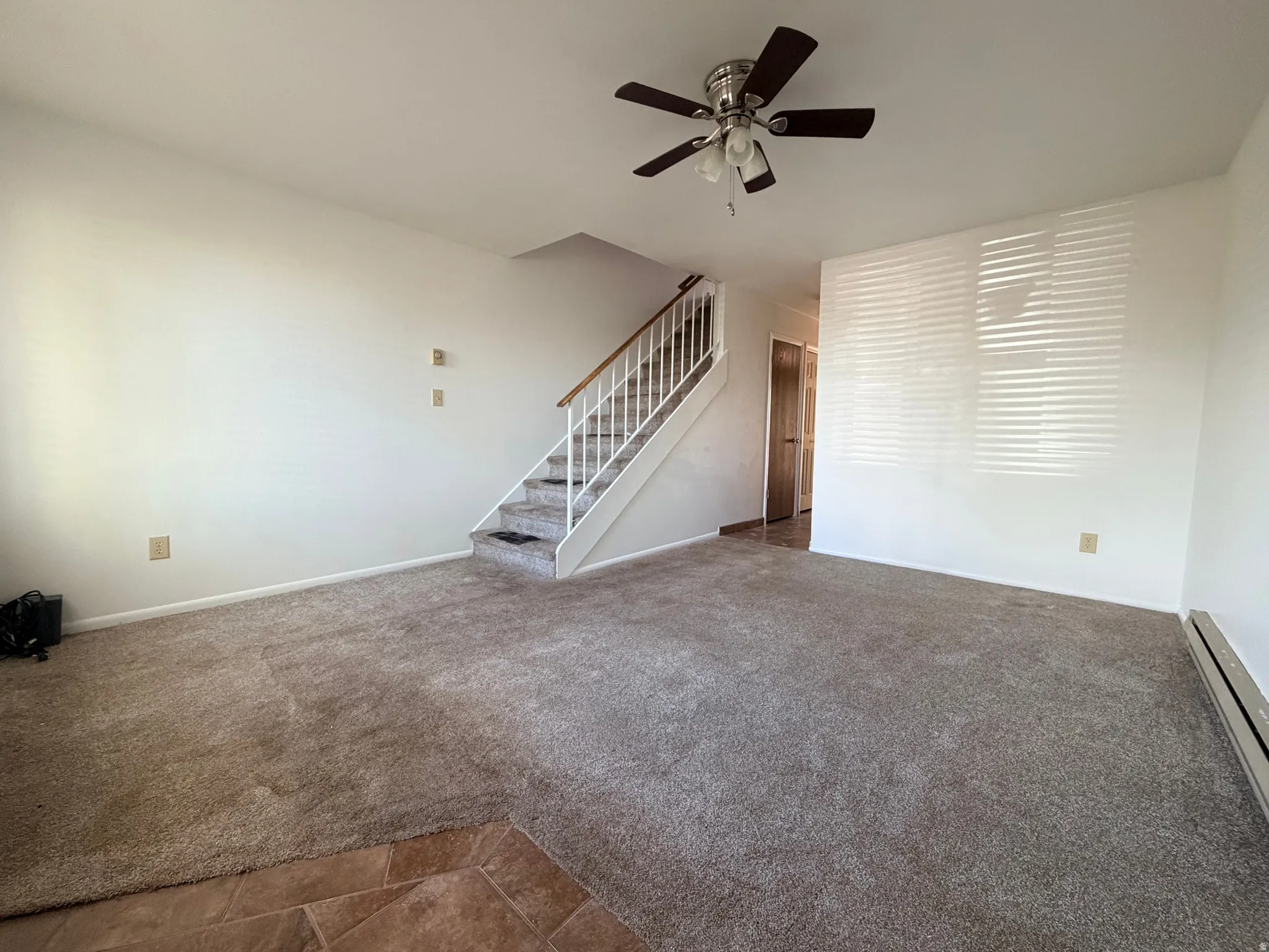 Unfurnished living room featuring a ceiling fan, dark carpet, and a baseboard heating unit